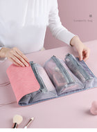 Pink multi-compartment mesh cosmetic travel bag with makeup brushes on a pink surface