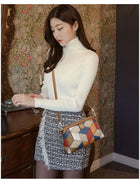 Woman in a white turtleneck and tweed skirt wearing a geometric patterned crossbody bag.