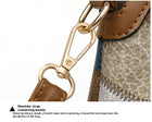Close-up of a gold-tone metal shoulder strap buckle on a textured brown and grey bag.