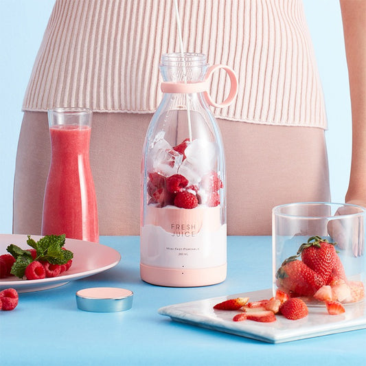 Pink portable blender bottle filled with fresh strawberry juice and ice cubes on a blue table.