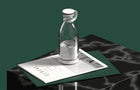 Clear glass juice bottle with white lid and carrying handle on a marble surface.
