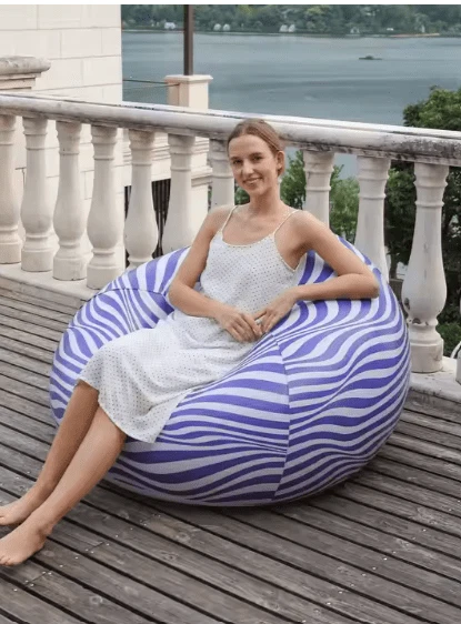 Woman relaxing on a blue and white striped outdoor bean bag chair on a wooden balcony.