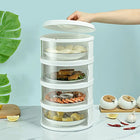 Multi-tier electric food steamer with white trays containing dumplings, meat, shrimp, and corn.