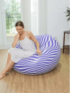 Woman relaxing on a purple and white swirl patterned bean bag chair in a bright room.