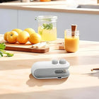 Portable electric handheld citrus juicer on a wooden kitchen counter with fresh lemons.