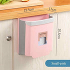 Small pink hanging kitchen trash bin attached to a wooden cabinet door.