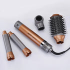 Rose gold hair dryer with round brush attachment and styling barrels.