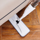 Handheld steam mop cleaning a wooden floor underneath a sofa