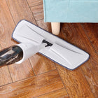 Handheld steam mop cleaning hardwood floor next to a light blue sofa leg