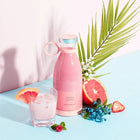 Pink portable juice bottle with a glass of pink smoothie, grapefruit, and berries on a blue surface