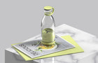 Clear glass juice bottle with a lime green cap and ring sitting on a magazine.