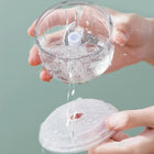 Hands rinsing a clear plastic manual food chopper with water.